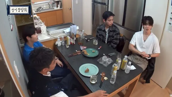 S.Coups sitting around a dining table, engaged in conversation. The table is set with plates of food, beverages, and utensils. The kitchen is visible in the background.