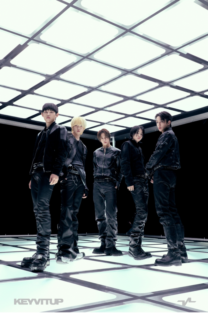 KEYVITUP in stylish black outfits pose confidently on a futuristic illuminated floor, with a bright, geometric ceiling overhead.