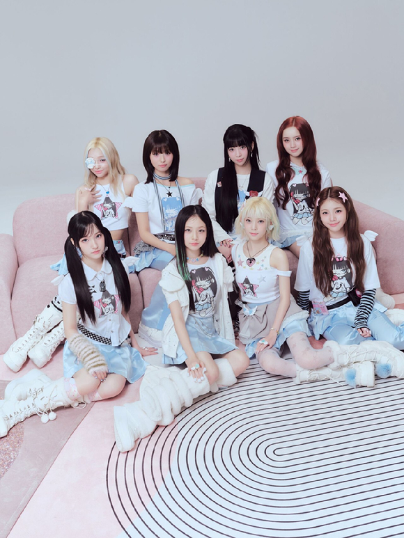 UNIS sitting on a pink couch, dressed in matching graphic t-shirts and skirts, with playful hairstyles and accessories, posing for the camera against a light background.