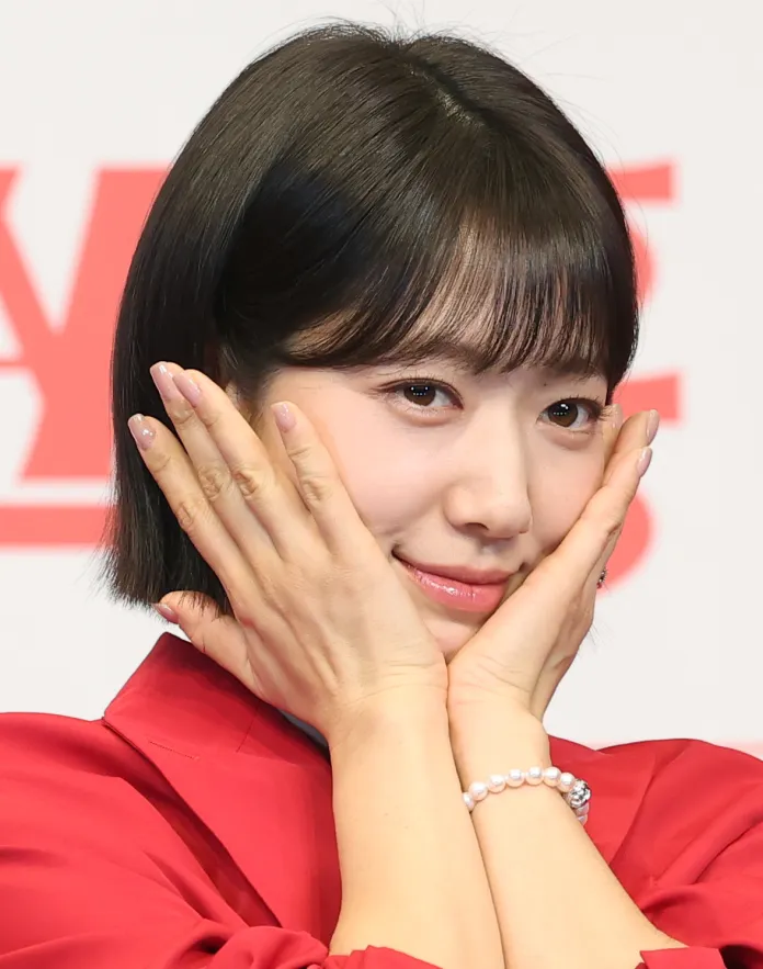 Park Shin-hye in a red outfit is playfully posing with her hands on her face, featuring a soft smile and styled dark hair.
