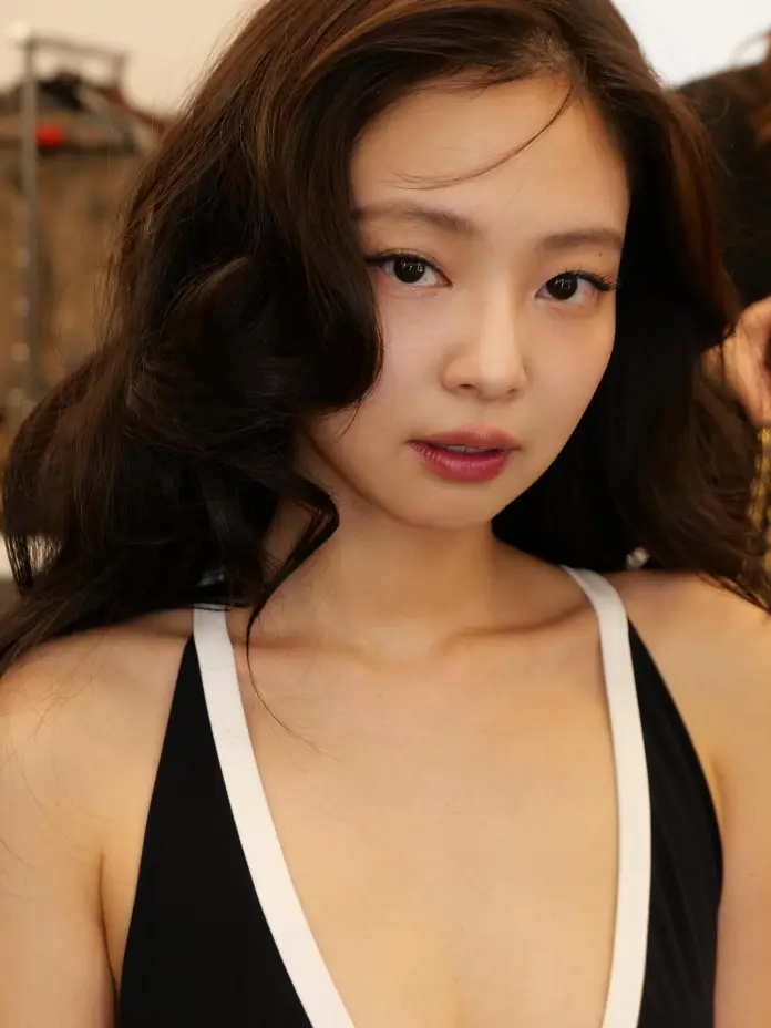Close-up portrait of a young woman with long, dark hair, wearing a black outfit with white accents, looking directly at the camera.