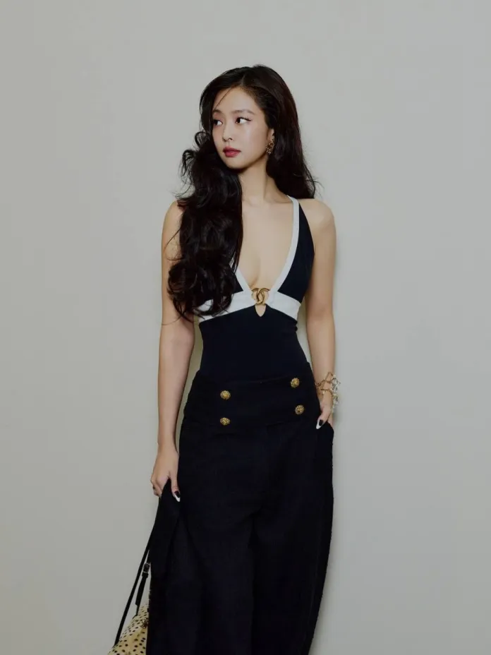 A woman with long, wavy hair wearing a black and white outfit featuring a deep V-neck and high-waisted trousers, posing against a neutral background.