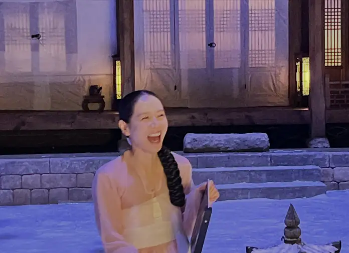 Son Ye-jin wearing a traditional outfit is laughing joyfully in front of a building with soft lighting, creating a warm atmosphere.