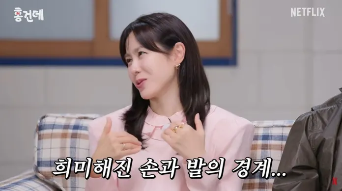 Son Ye-jin with long dark hair in a pink blouse smiles while talking, seated on a plaid couch. Text in Korean appears at the bottom.