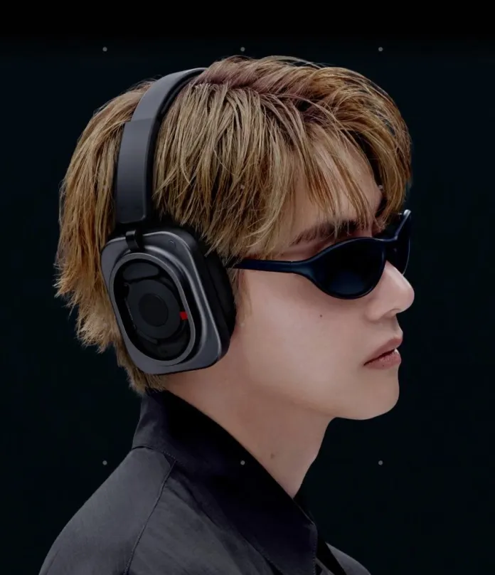 Kim Taehyung with stylish blonde hair, wearing black headphones and dark sunglasses, against a black background.