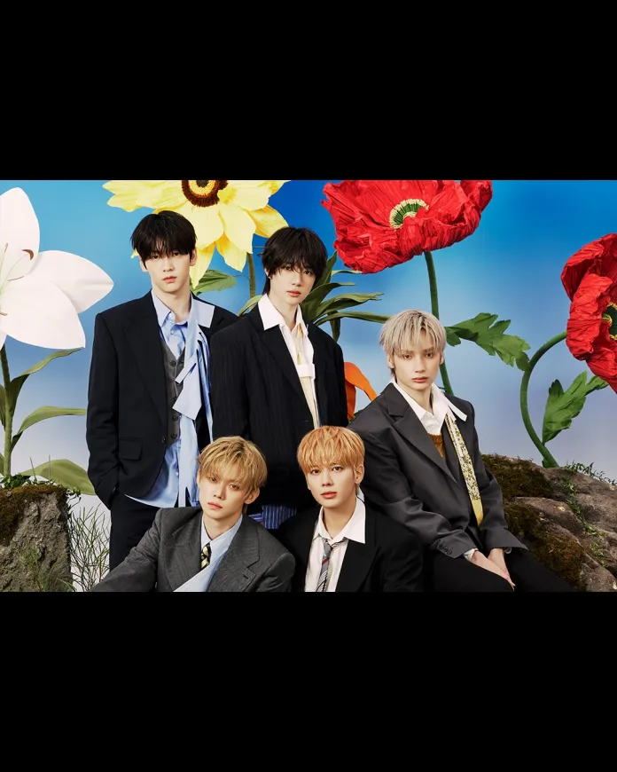TXT members in stylish suits, posing in front of oversized, vibrant flowers against a blue sky backdrop.