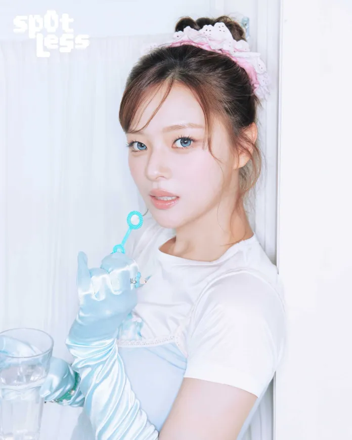 Jeongyeon with long hair styled in a bun, wearing a pink headband and blue gloves, holding a bubble wand and a glass of water, standing in front of a white curtain.