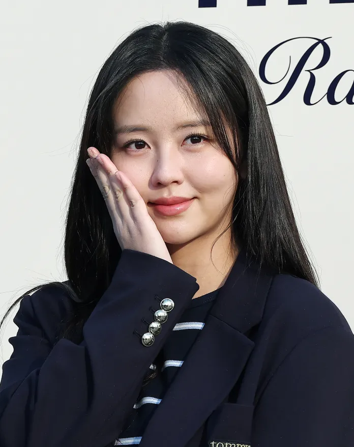 Kim So-hyun with long black hair touching her face, wearing a navy blazer over a striped shirt, smiling softly against a light background.