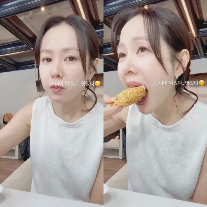 Son Ye-jin  enjoying a piece of fried chicken while seated in a casual dining setting. Son Ye-jin appears content, with a close-up of her taking a bite.
