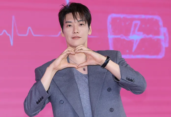 A person in a stylish gray blazer making a heart shape with their hands against a pink background with a heartbeat line and a battery icon.