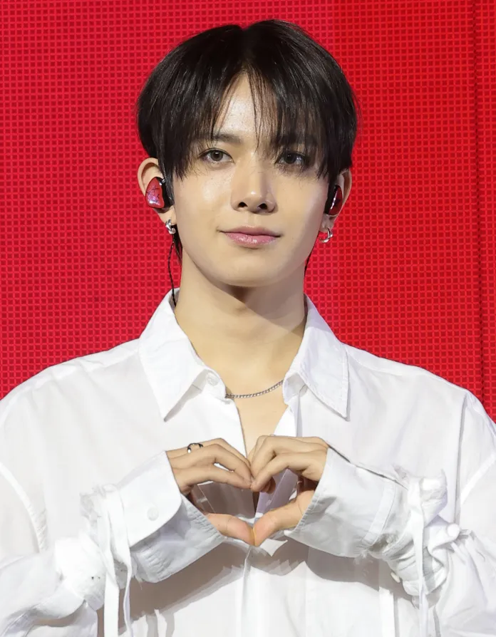 A person in a white shirt making a heart shape with their hands against a red background.