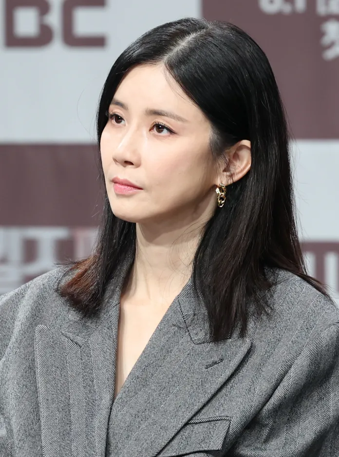Close-up of Lee Bo-young with straight black hair, wearing a grey patterned blazer, looking thoughtfully off-camera.