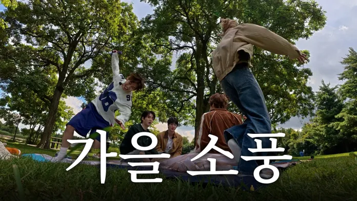 BTS enjoying a picnic outdoors under trees, with one person joyfully leaping in the foreground. The background features lush greenery and a clear blue sky.