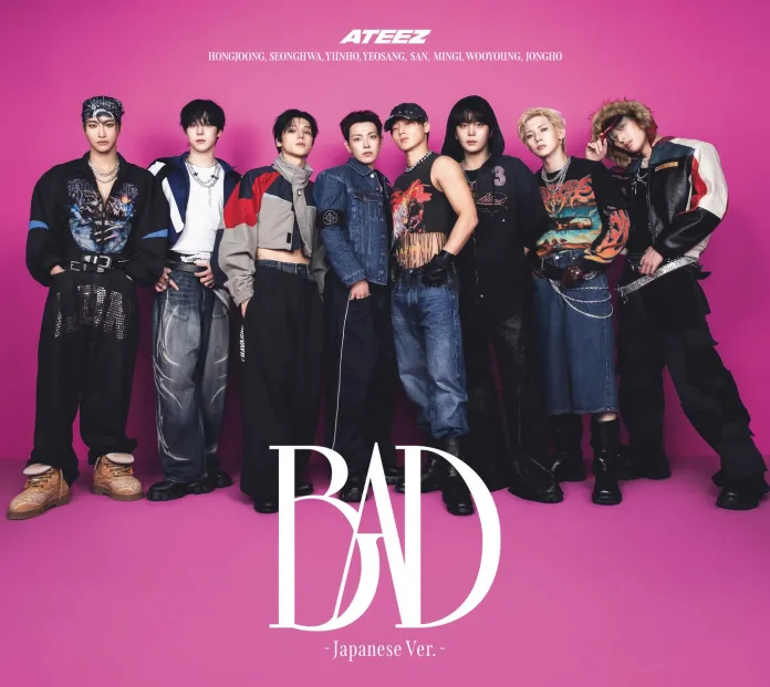 A group of nine young men from the K-pop group ATEEZ poses against a vibrant pink background, dressed in trendy streetwear. They are featured in a promotional image for their Japanese version of the song 'BAD.'