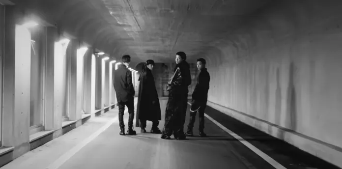 LNGSHOT members standing in a dimly lit tunnel with a smooth road surface, dressed in dark, stylish clothing.