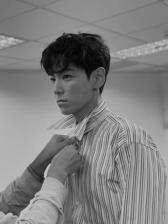 T.O.P with curly hair is getting his shirt collar adjusted by another person in a studio setting.