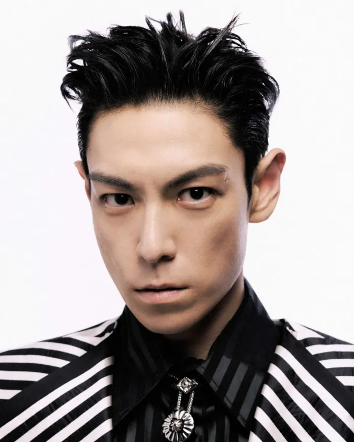 T.O.P with styled black hair, wearing a striped shirt with a decorative collar, against a plain white background.