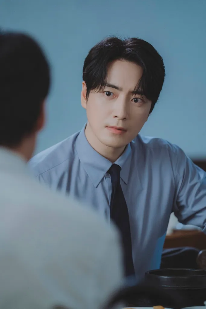 Lee Jun-hyuk in a light blue dress shirt and tie is listening intently during a conversation, showcasing an expression of concern or focus.