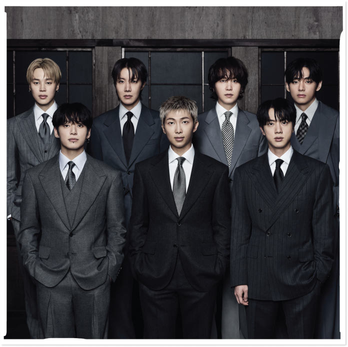 A group photograph of seven individuals dressed in stylish suits, posing confidently in a dimly lit setting with a modern backdrop.
