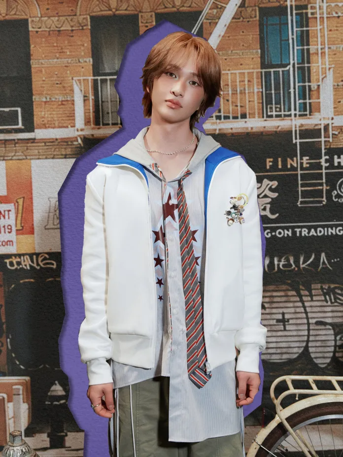 Onew stands confidently in front of a colorful urban backdrop, wearing a white jacket with blue details, a patterned shirt, and a striped tie. The background features a mix of graffiti and urban architecture.