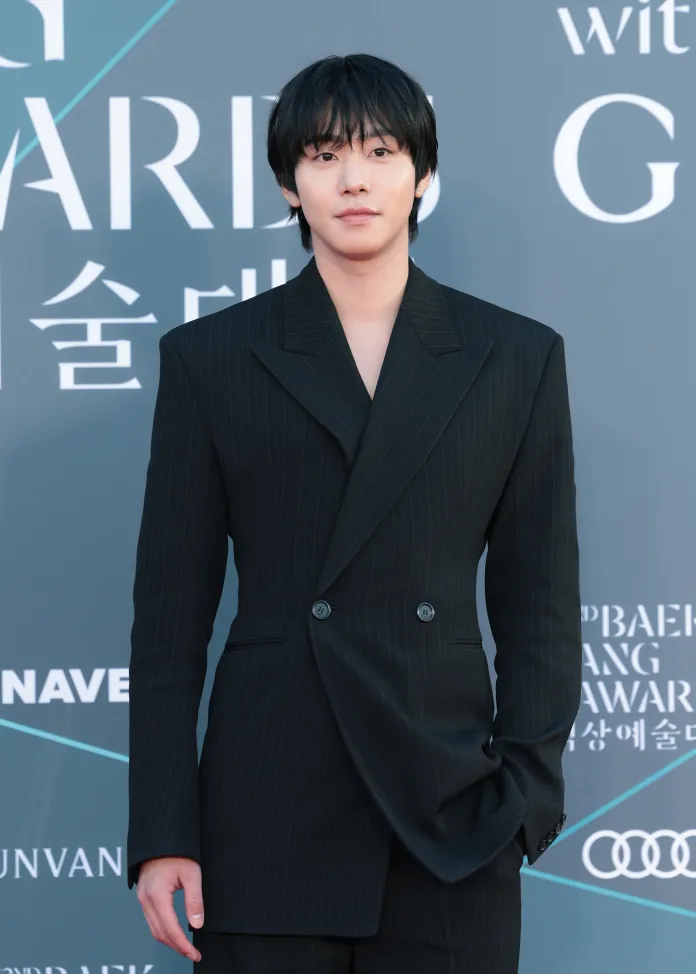Ahn Hyo-seop in a tailored black pinstripe suit at a formal event, posing confidently against a backdrop with award signage.