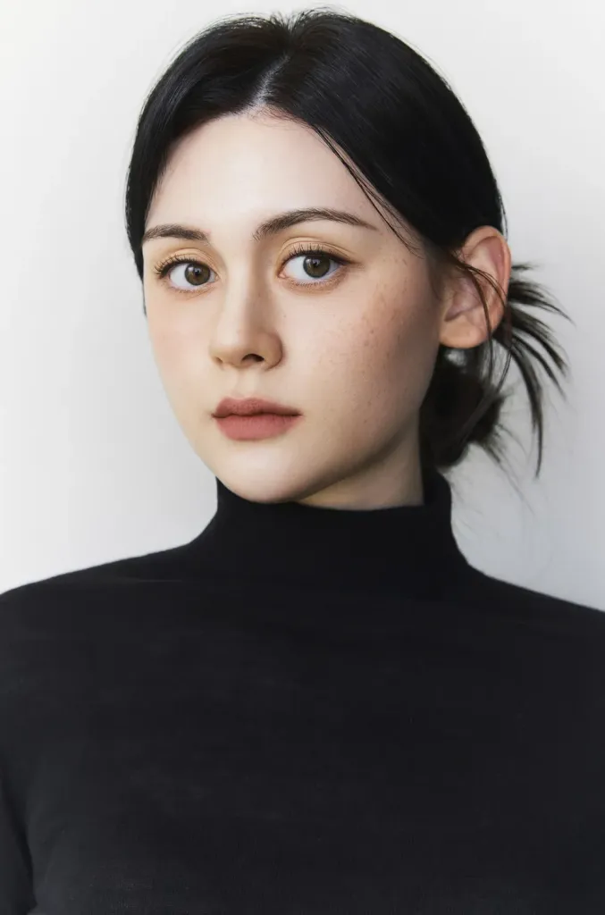 Portrait of Hailey with dark hair and a turtleneck sweater against a light background.