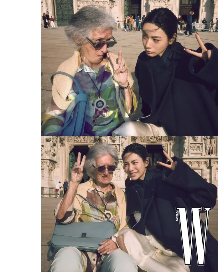 Nana and an older woman pose together, both making peace signs with their fingers in front of a historical building.