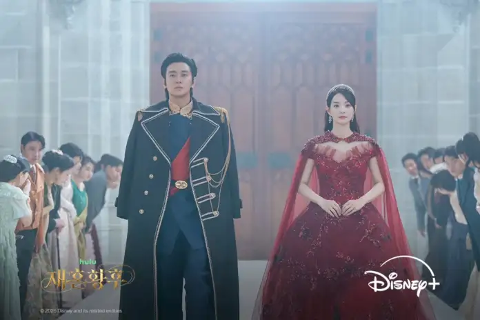 Shin min ah and Ju jihoon stands confidently in a grand hall, surrounded by onlookers. The man is dressed in a military-style uniform with a long coat, while the woman wears an elegant red gown with a matching cape.