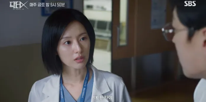 Kim Ji-won in a white lab coat, with short black hair, is having a serious conversation with a male colleague, who is wearing glasses. They appear to be in a hospital setting.