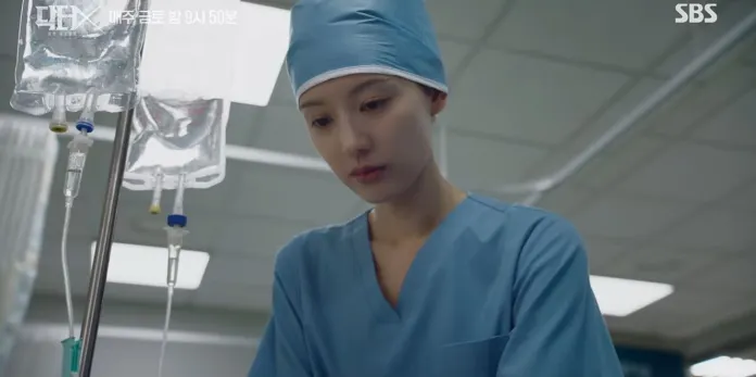Kim Ji-won in scrubs and a surgical cap focuses on medical equipment in a hospital setting.