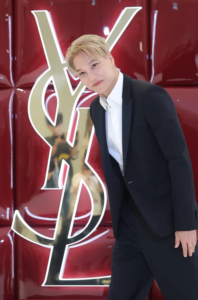 EXO's Kai individual in formal attire standing in front of a glossy red backdrop featuring the Yves Saint Laurent logo.