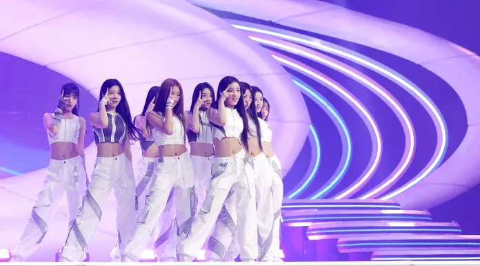 A2O LITE performing on stage, wearing matching white outfits with colorful lighting in the background.