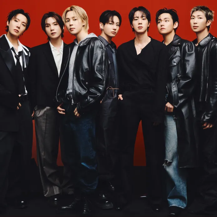 BTS dressed in fashionable black and gray outfits, posing together in front of a red background.