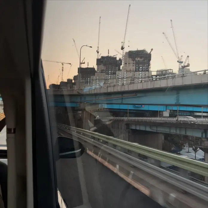 View from a vehicle showcasing a multi-level highway and construction cranes over buildings at sunset.