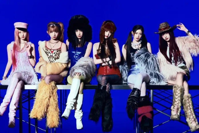A group of six individuals posing on a metal bench against a blue background, dressed in vibrant, fashionable outfits with a mix of textures and colors, showcasing unique hairstyles and accessories.