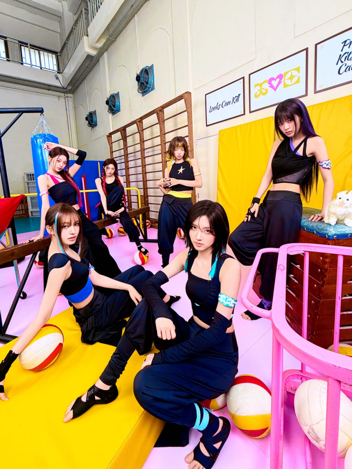 A group of five young women poses playfully in a colorful indoor setting, wearing stylish athletic attire. They are surrounded by colorful sports equipment, including volleyballs, and are situated against a backdrop of vibrant walls and gym apparatus.