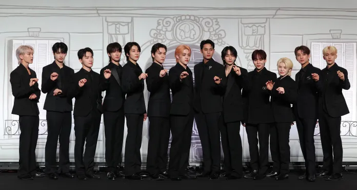 A group photo of SEVENTEEN members dressed in matching black outfits, posing confidently with playful expressions against a decorative background.