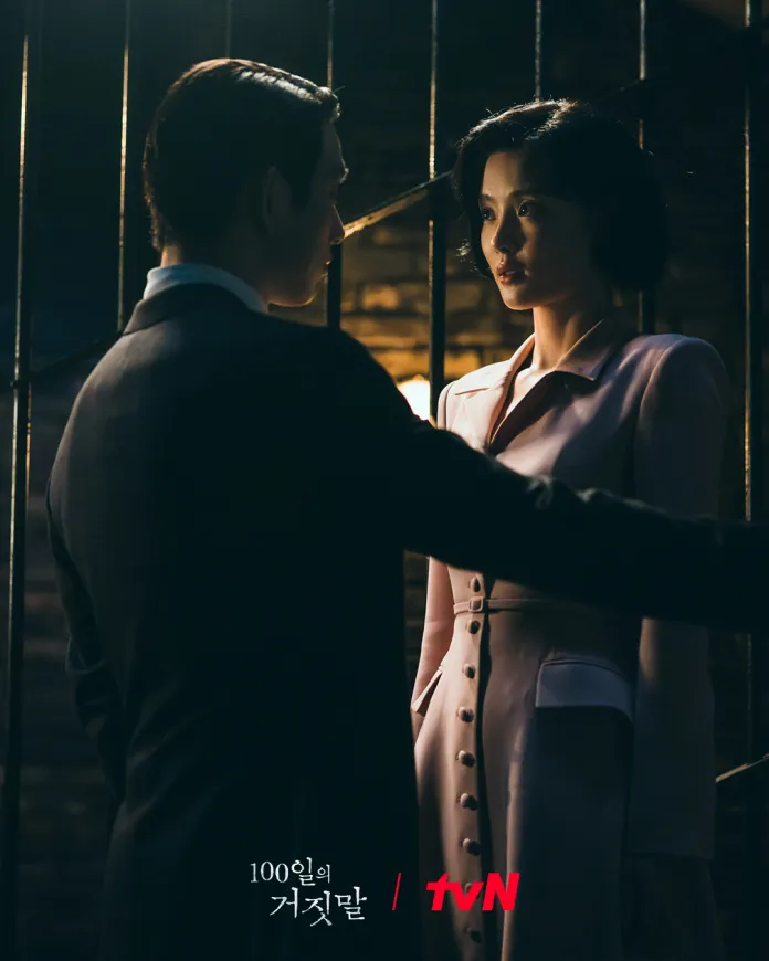 A dramatic moment between Kim Yoo-jung and Park Jinyoung in a dimly lit setting, featuring Park Jinyoung in a suit and Kim Yoo-jung in a pink coat, both looking at each other intently.