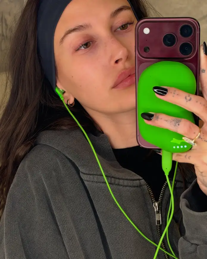 Close-up selfie of a person wearing a black headband and a gray hoodie, with green earbuds connected to a smartphone case.
