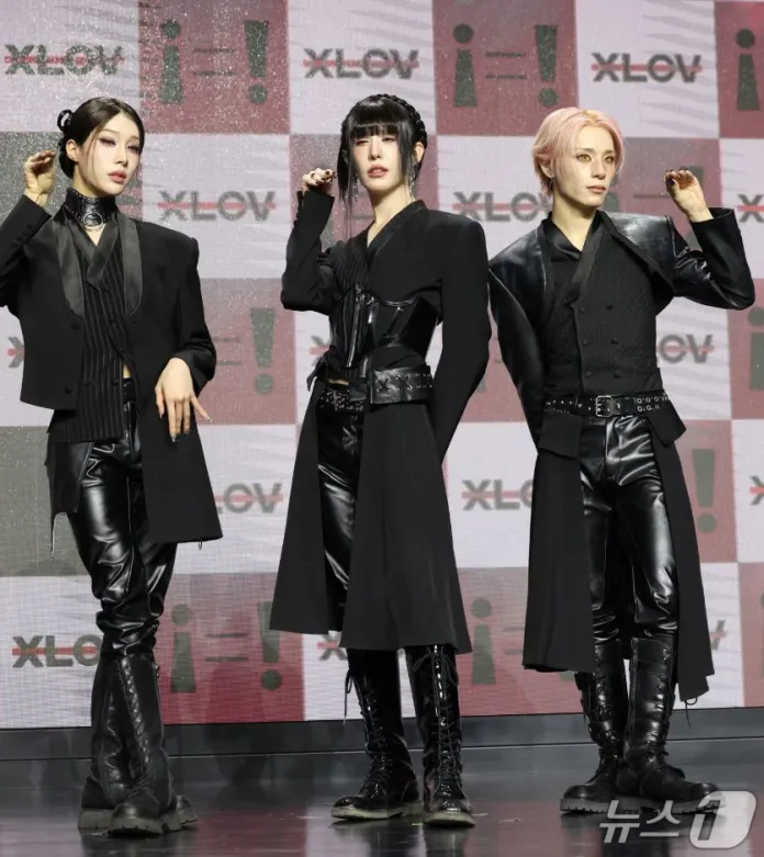 XLOV in stylish black outfits posing confidently on a stage, with a backdrop featuring the logo 'i! XLOV'.