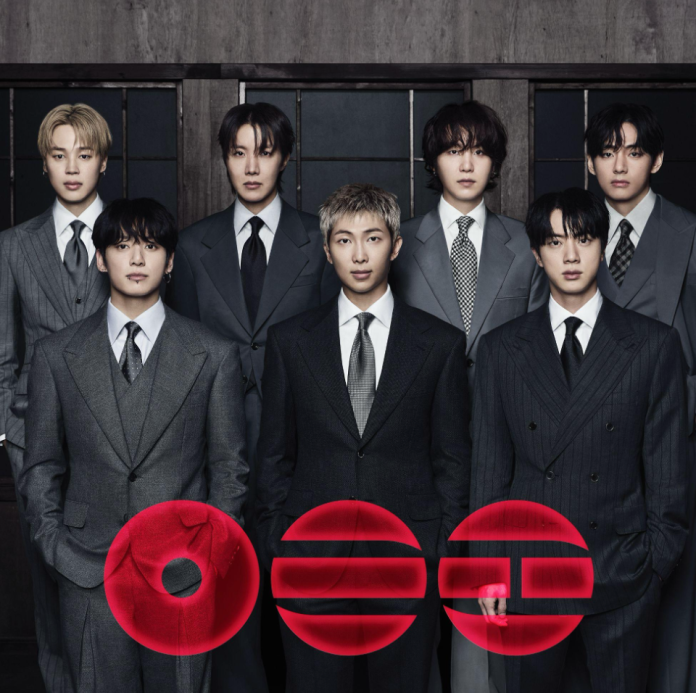 BTS wearing formal suits, standing in two rows against a dark background. They appear serious and composed, with distinct hairstyles and outfits. The image features a stylized logo in red at the bottom.