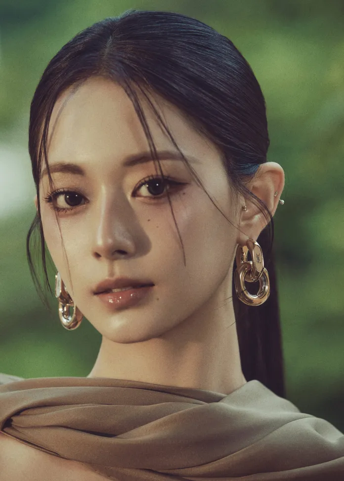 Tzuyu with long, dark hair wearing large hoop earrings and a flowing brown scarf, set against a blurred green background.
