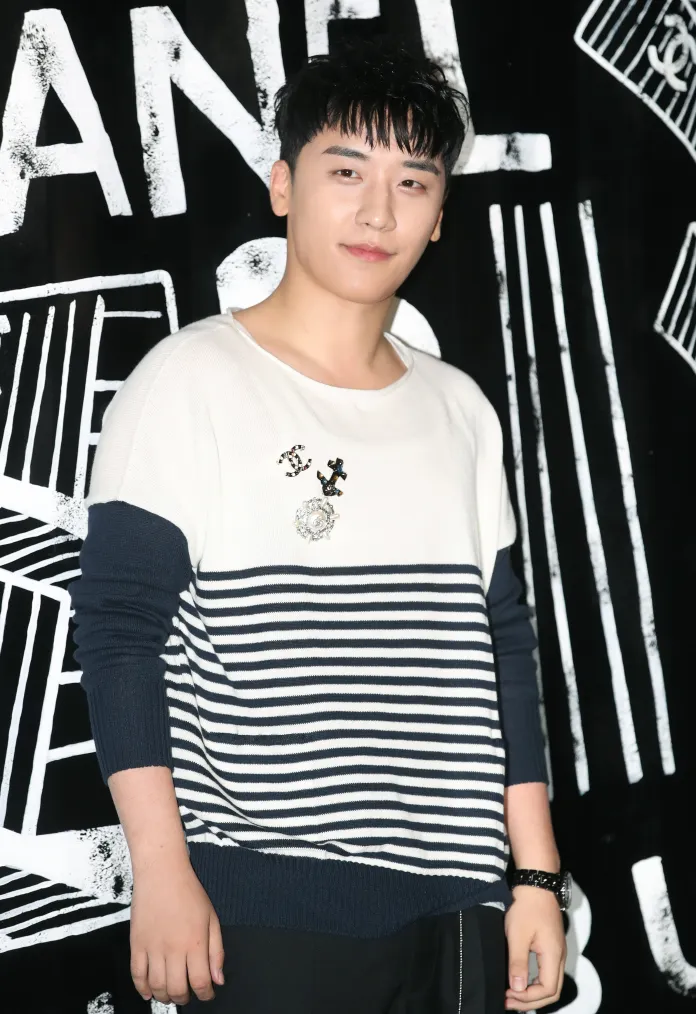 Seungri posing in front of a black and white background with Chanel branding, wearing a striped sweater and smiling.