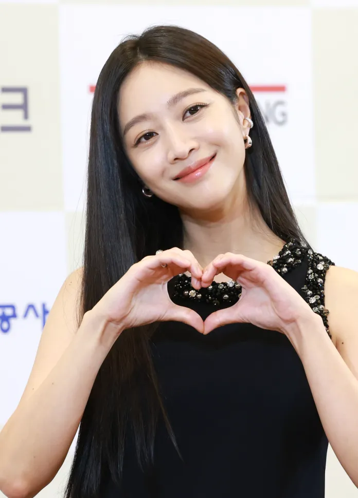 Jo Bo-ah with long dark hair smiles while making a heart shape with her hands, wearing a black dress with embellishments.