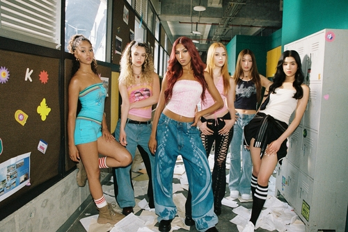 KATSEYE posing together in a colorful indoor setting, wearing stylish outfits including crop tops, jeans, and athletic socks, with a backdrop of lockers and scattered papers.