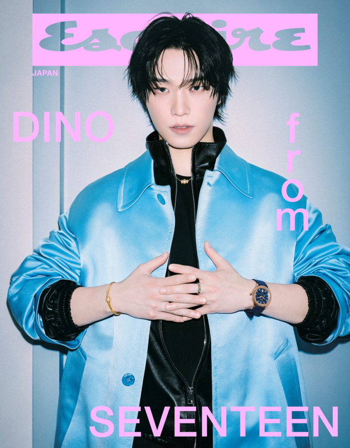 SEVENTEEN’s Dino poses confidently in a stylish light blue jacket, showcasing a modern and edgy fashion sense. He is wearing accessories, including bracelets and a watch, and has a serious expression. The background is minimalistic, with the word 'Esquire' prominently displayed.