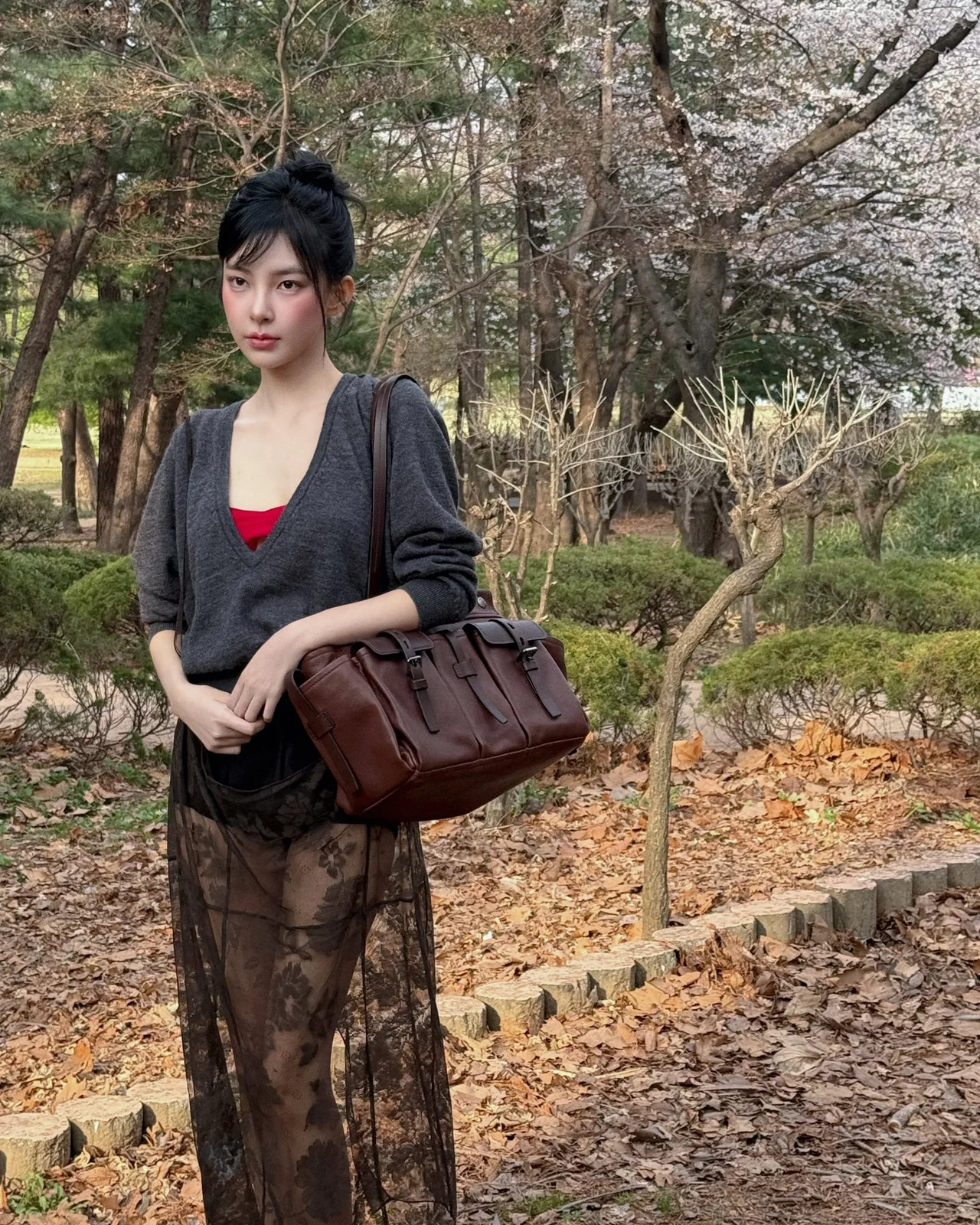 벚꽃 공원에서 그레이 니트와 블랙 레이스 스커트, 버건디 백으로 다크 시크 룩을 완성한 모습 /사진=신수현 인스타그램