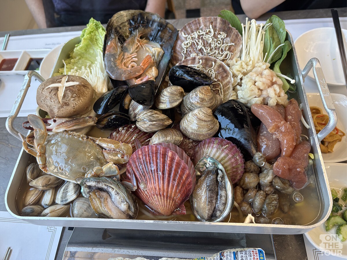 조개와 전복, 새우 등 해산물이 냄비 가득 담겨 있다. / 온더투어