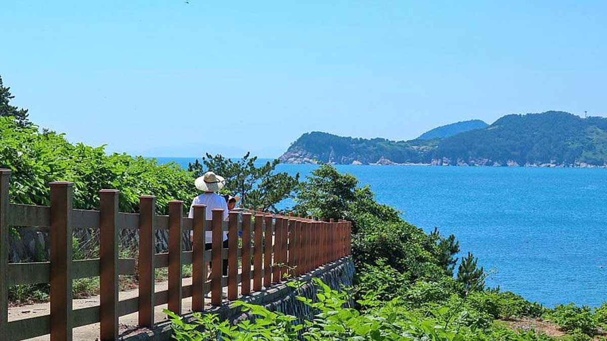 비진도 해안 산책로에서 한려수도 바다와 섬들이 내려다보이고, 관광객이 바다를 따라 난 길을 걷고 있다. / 한국관광공사