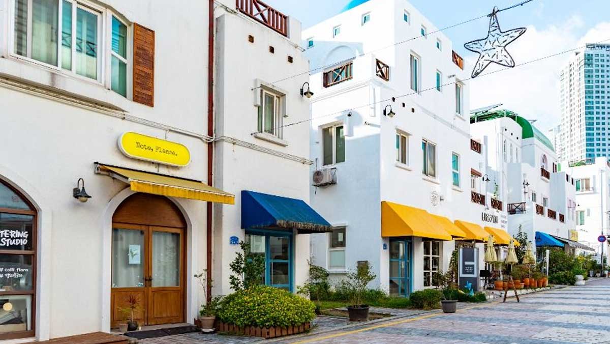 아산 지중해마을 1층 상가 거리. 흰 건물 아래 카페와 소품점, 노란 차양이 골목을 따라 이어져 있다. / 한국관광공사